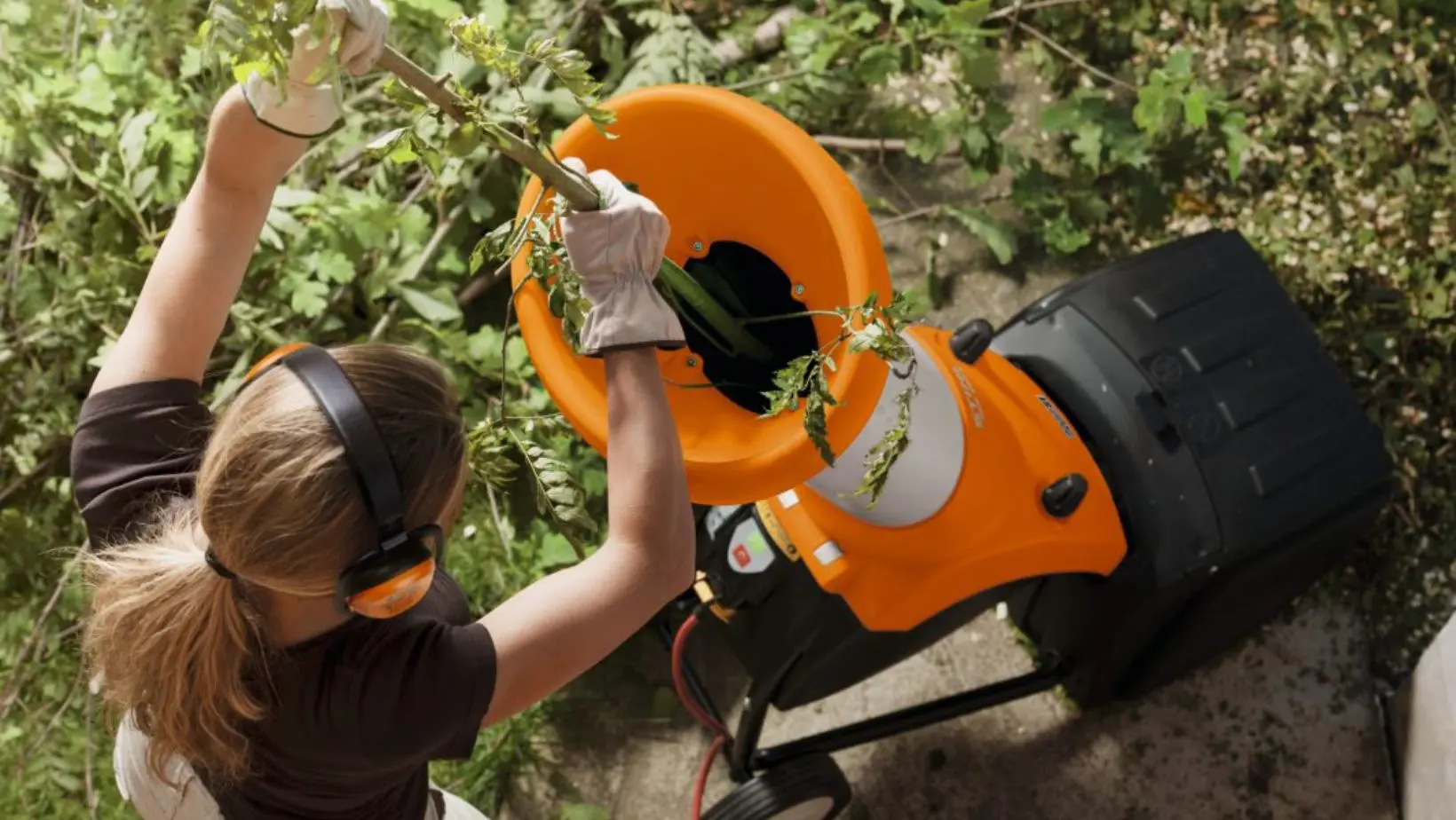 a woman putting a branch in an electric chipper shredder