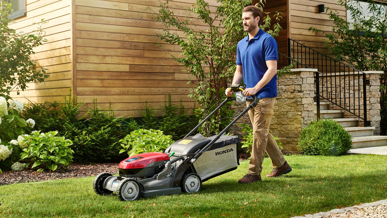 Honda_HRX_Location 01-min a man in a blue top pushing a lawnmower past a house