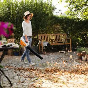 a woman using a leaf blower to prepare a garden for winter