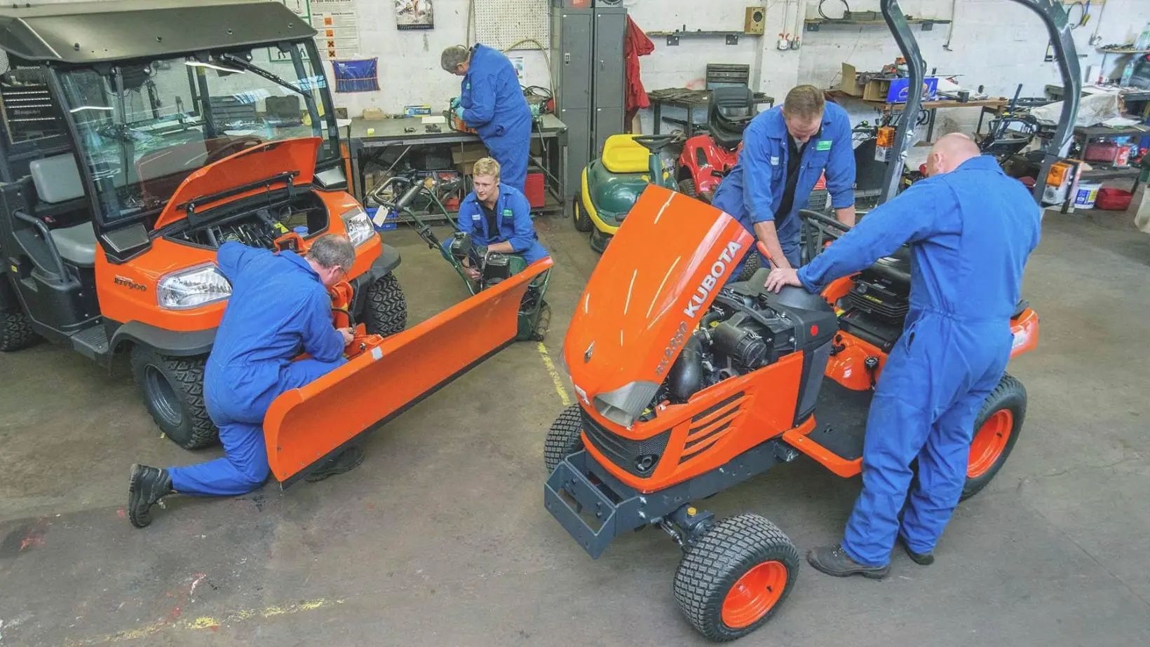 mechanics in blue overalls carrying out garden machinery services on orange ride-on mowers