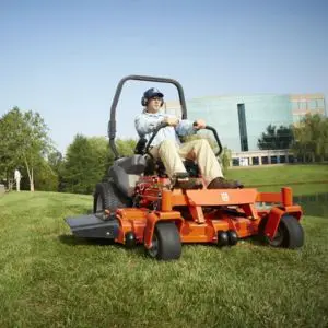 a man riding an orange zero turn mower across a park