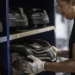 a male service technician, wearing gloves, taking a robot mower off a shelf 