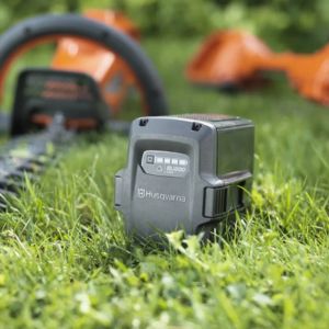 a garden machinery battery sat on a lawn, with a garden power tool in the background