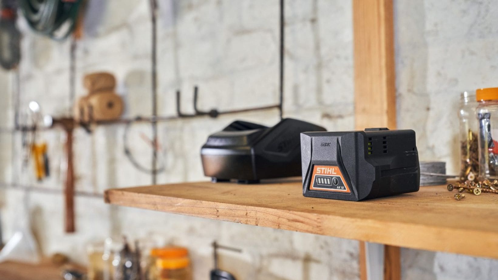 a garden machinery battery and charger, in a garage, on a wooden shelf