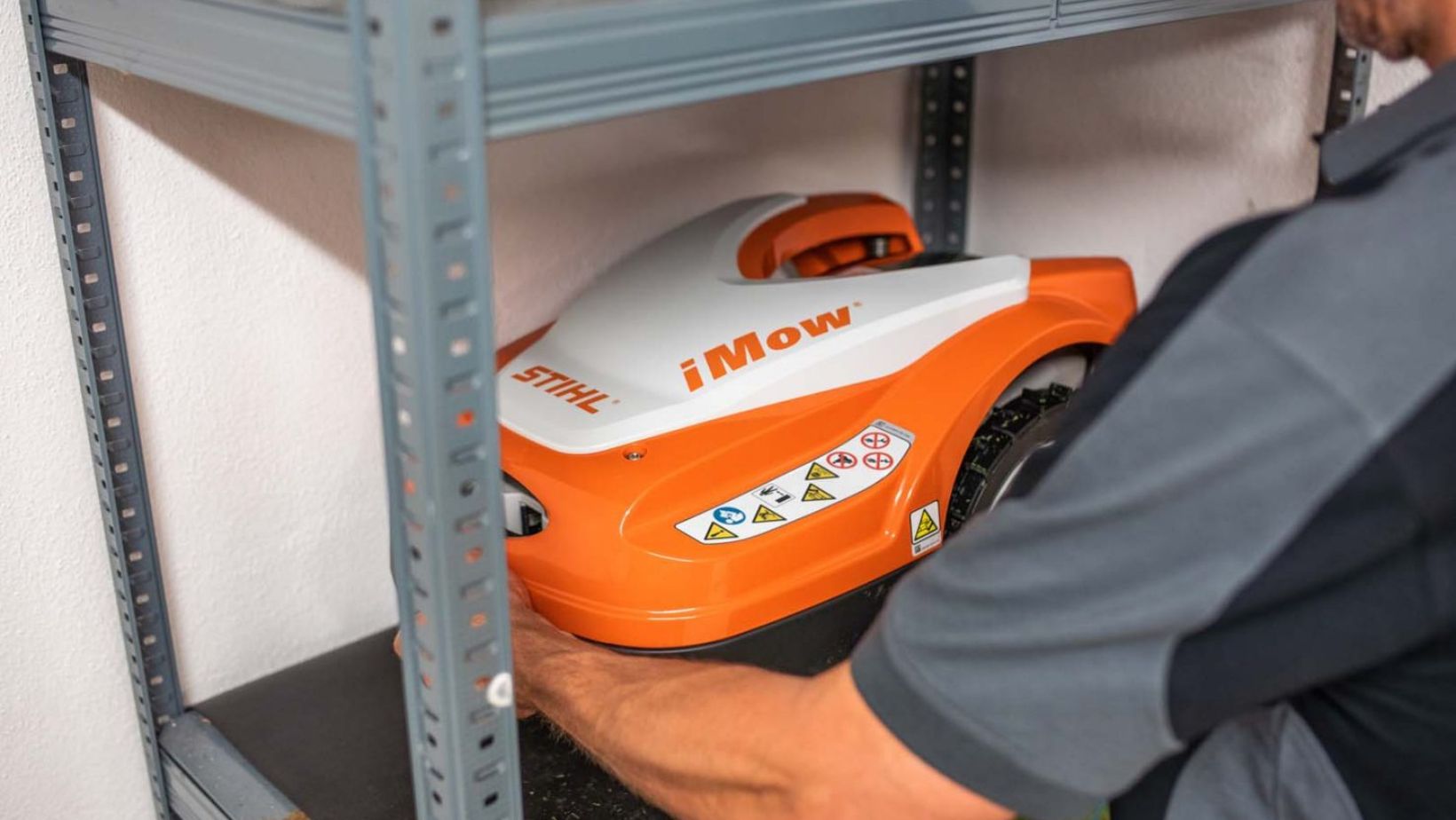 a man putting an orange and white STIHL robot mower on a shelf for winter storage
