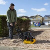 a man using the Handy THLC29140 Petrol Plate Compactor to lay the foundations for a driveway