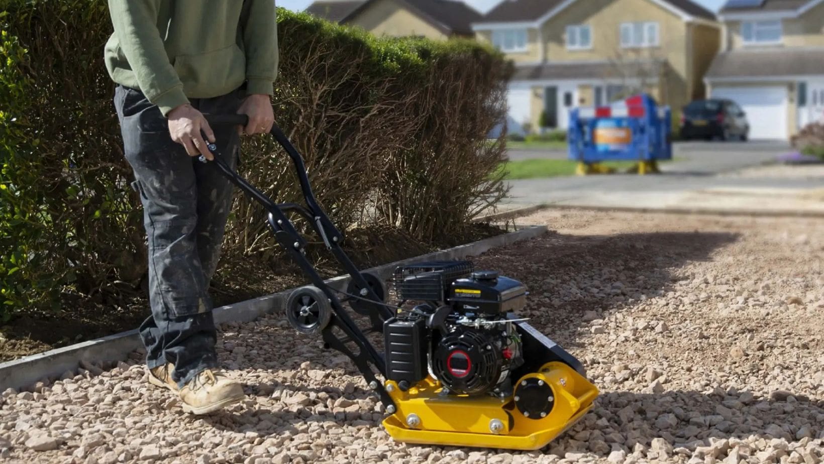 a man compacting the soil on the foundations for a driveway, using a Handy THLC29140 Petrol Plate Compactor