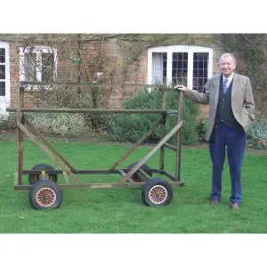 a smartly dressed man stood next to a wheeled ladder platform, in a garden