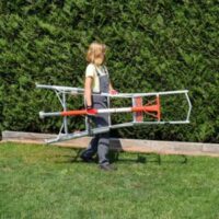 a woman carrying a Henchman Professional Tripod Ladder across a garden