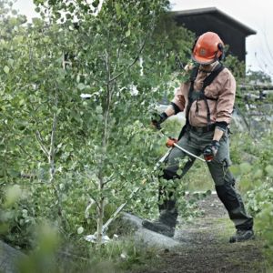 a man wearing PPE including a helmet, gloves and boots, operating a brush cutter