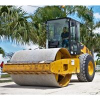 a man driving a steamroller along a road, with palm trees in the background