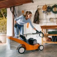 a woman getting a lawnmower out of the garage