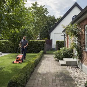 a professional gardener mowing a lawn, with a hedge and house to the right of the picture