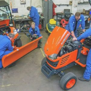 mechanics in blue overalls servicing 2 lawn tractors in a workshop