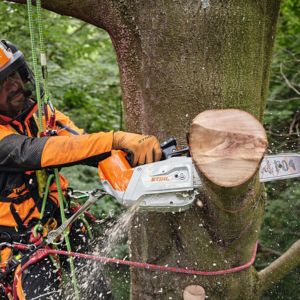 a man in orange PPE, cutting a thick branch off a tree, using a powerful chainsaw