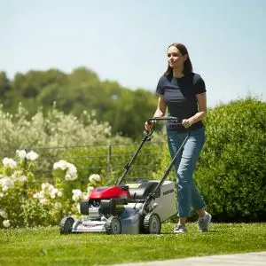 a woman mowing a lawn, with plants, shrubs and trees in the background