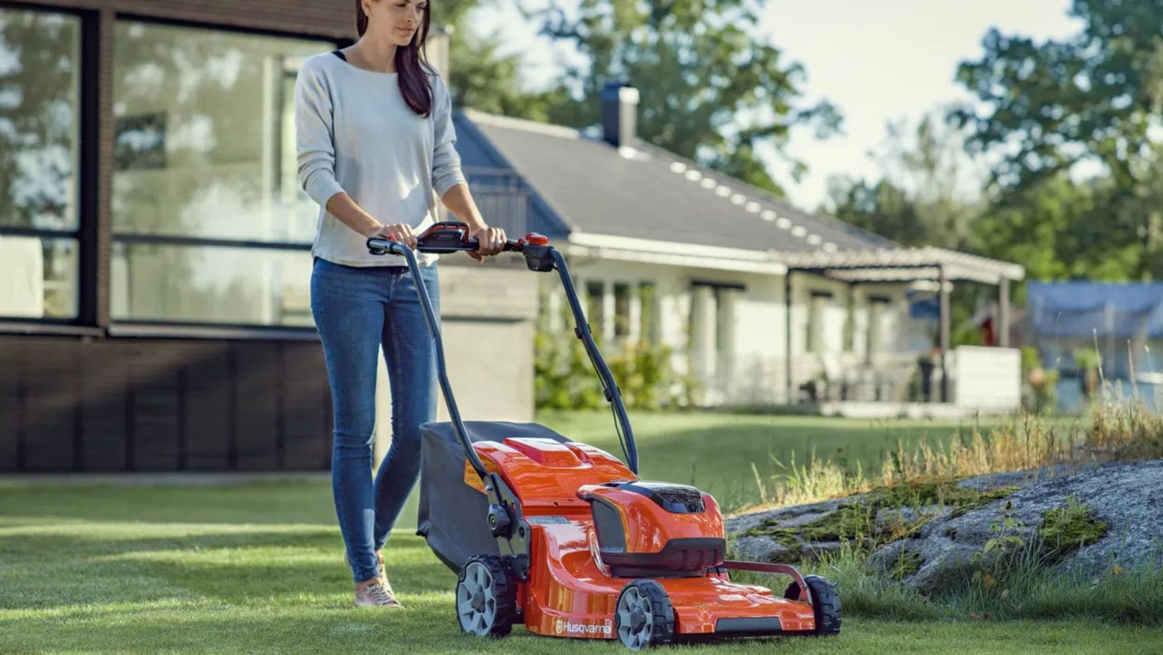 Husqvarna lawnmower-min a woman mowing the lawn using an orange Husqvarna lawnmower, with a bungalow in the background
