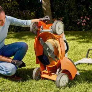 a woman showing the underside of a lawnmower to demonstrate how to measure a lawn mower width