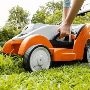 someone setting the cutting height on an orange and white STIHL lawnmower