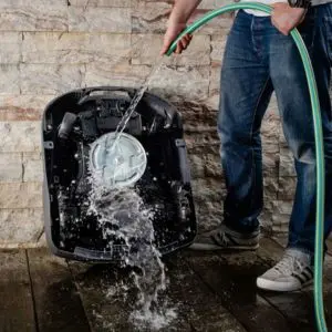 a man cleaning the underside of a robotic lawnmower, using a garden hose