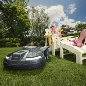 an elderly woman in sunglasses, holding a drink, lay on a sun lounger, smiling at a robotic mower