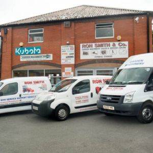 3 white vans parked outside a red-brick building, all of which are displaying Ron Smith advertisements