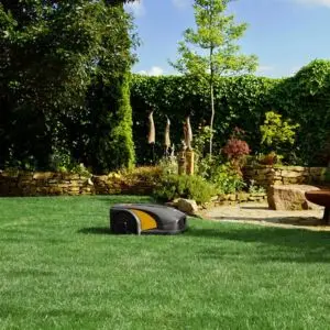 a STIGA A 5000 Robotic Lawnmower on a lawn, with trees and shrubs in the background