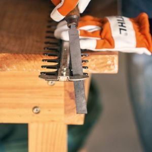 someone wearing STIHL gloves, using a flat file to sharpen a hedge trimmer's blade