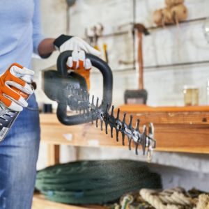 someone spraying a resin solvent onto a hedge trimmer's blade to lubricate and protect it