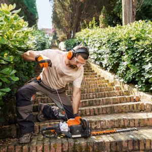 a man pulling the starting cord of a petrol hedge trimmer, which is sat on the bottom of a series of steps in the garden