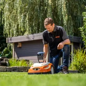 a male STIHL technician making adjustments to a STIHL iMow robotic lawnmower in a garden