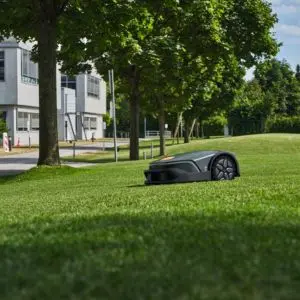 a STIHL iMOW® 7 PRO Robot Mower travelling down a gentle slope towards trees, a road and housing