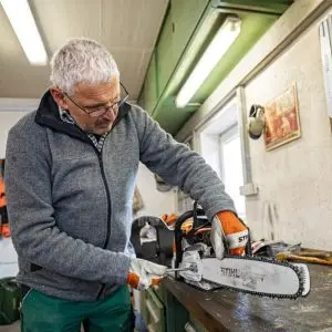 a man wearing glasses tensioning the chain on a STIHL chainsaw