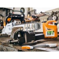 a petrol chainsaw in a vice, on a wooden workbench, surrounded by tools and bottles of fuel