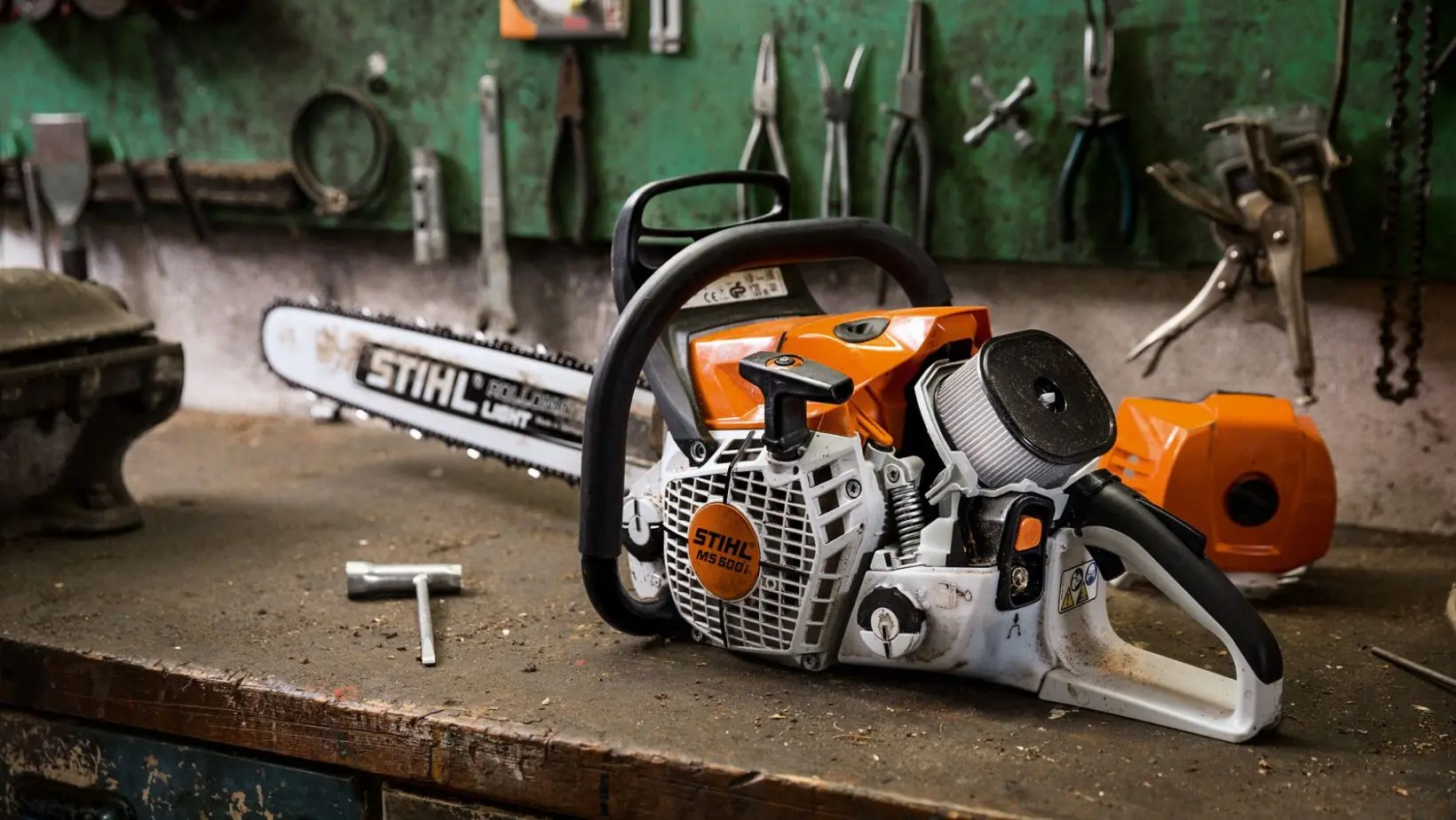 a STIHL MS500i Petrol Chainsaw on a wooden workshop bench, with tools hanging on the wall behind it