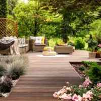rattan garden furniture on wooden decking, surrounded by shrubs and trees