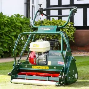 the Allett Buckingham 24H Petrol Cylinder Mower on a striped lawn, in front of hedging and a mock Tudor house