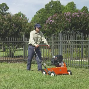 a man in a baseball cap using a Husqvarna scarifier on a lawn