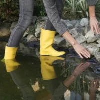 a woman in yellow wellies, carrying out pond maintenance in September
