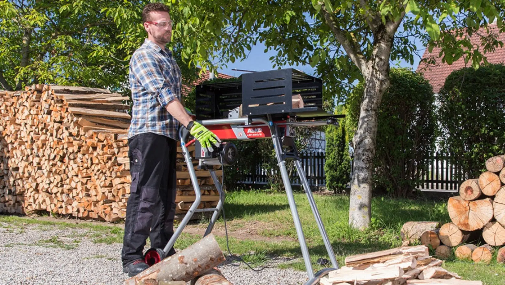 a man in a garden, stood near a large pile of logs, operating the AL-KO Easy LSH 5205 Electric Log Splitter