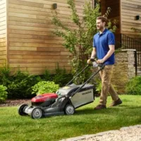 a man mowing a stretch of lawn between a wooden house and gravel path, using a Honda HRX Lawnmower