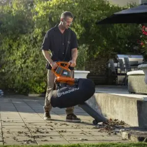 a man vacuuming up leaves near a step, using the Husqvarna 120iBV Cordless Leaf Blower & Vacuum Shredder