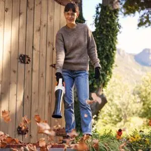 a woman stood near a garden fence using the STIHL SHA 56 Cordless Vacuum Shredder to blow leaves