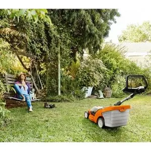 a woman relaxing in a garden, on a swinging wooden bench, underneath a tree, with an orange and white STIHL lawnmower parked on her lawn