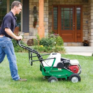 a man using the Billy Goat AE401H Petrol Lawn Aerator on a lawn outside a house