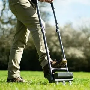 a man stood on a lawn, using his foot to press the Handy THHTA Aerator into the turf