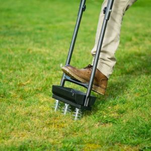 a close up of a man stepping on the Handy THHTA Hollow Tine Aerator to aerate a lawn
