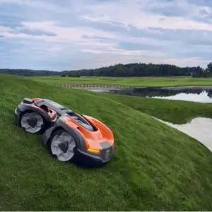 the Husqvarna Automower® 535 AWD Robotic Mower cutting grass on a very steep hill, with a lake in the background