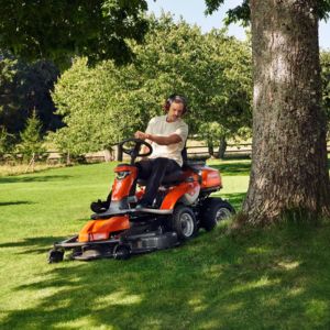 a man operating the Husqvarna R 316TsX AWD Rider on a slightly sloping lawn, near a tree