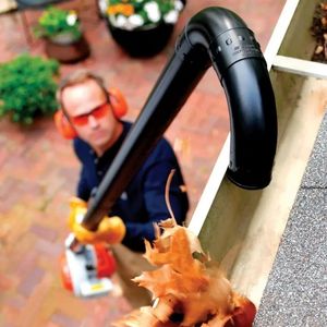 a man wearing protective glasses and ear defenders, stood on a patio, using a STIHL blower and gutter cleaning kit to remove dried leaves from a first-floor gutter